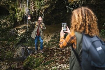 wife take a photo of husband backpacker in front cave in the forest