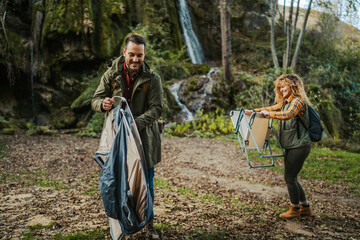 Hiker couple set up camp near waterfall in autumn forest scene