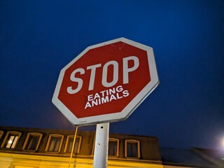 A unique traffic sign reading "STOP EATING ANIMALS," symbolizing a call for vegetarianism, veganism, and ethical dietary choices in a creative urban art format.