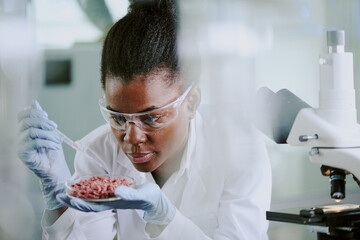 Scientist wearing protective gear analyzing tissue samples under microscope in laboratory environment with concentration and precision