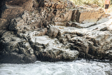 A solitary person gazes at the flowing river from rocky formations, surrounded by nature's beauty, while the sun dips low, casting a warm glow on the landscape.