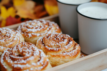 Delicious cinnamon rolls, dusted with pearl sugar, served with two mugs of milk, creating a cozy autumnal scene