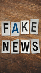 Fototapeta premium The word FAKE NEWS is spelled out using individual letters cut from a newspaper, arranged on a wooden surface.