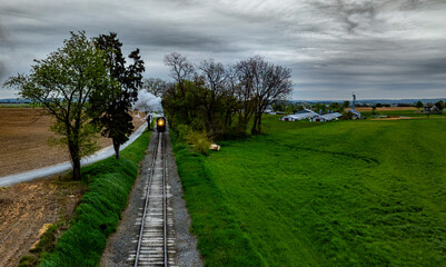 A Vintage Steam Locomotive Travels Through Lush Greenery Near a Rural Farm on a Cloudy Day