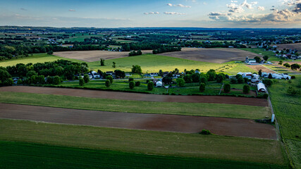 Obraz premium The landscape showcases expansive farmland with vibrant fields, quaint homes, and patches of greenery illuminated by the soft glow of the golden hour, depicting rural life in the countryside.