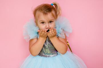 Girl with long hair in festive paper hat and dressy dress on pink background tossing gold confetti