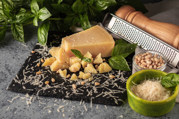 Gourmet Italian Parmigiano Reggiano with Basil and Pine Nuts: Aged Cheese Slice on Black and Wooden...