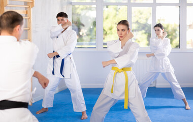 Diligent young woman attendee of karate classes practicing kata standing in row with others in...