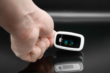 Hand holding digital pulse oximeter with displayed readings on dark background