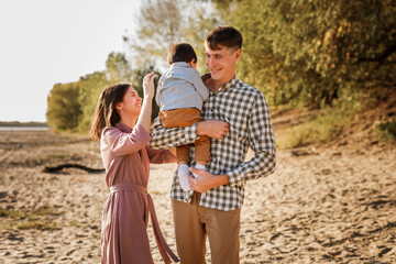 Naklejka premium Happy family walking on the road in the park. Father, mother holding baby son on hands and going together. Rear view. Family Ties concept.