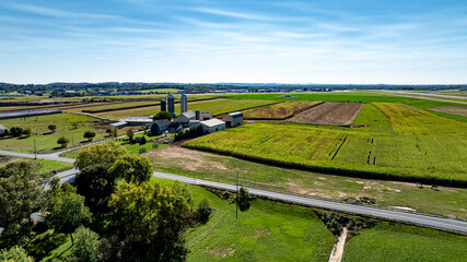 An expansive farm stretches across the landscape featuring lush fields, silos, and a winding road...
