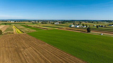 A vast expanse of farmland stretches across the landscape, featuring green fields and cultivated...