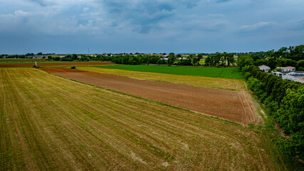 A field with a mix of green and brown grass. The sky is cloudy and the sun is not visible
