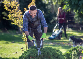 Man and woman taking care of garden in autumn time, trimming bushes and mowing lawn