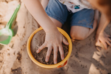 child patting sand in bucket