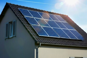 Fototapeta premium A house roof with solar panels under a bright sun.