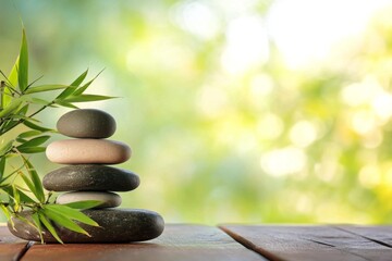 Zen stone stack with bamboo leaves on wooden table, serene spa concept banner with green background and ample copy space, capturing tranquility in boho style with smooth natural light.