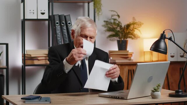 Caucasian senior businessman opening envelope reading bad news in letter feels upset sitting at home office desk. Financial problems, bank debt bill for pay, tax invoice or bankruptcy notification.