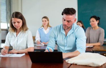 Obraz premium Guy student, studying at the same desk with a girl fellow student in a university auditorium with a group, studies on a laptop ..and writes a synopsis in a copybook