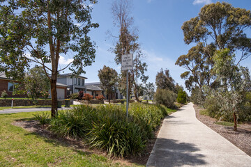 A well-maintained walking path winds through a tranquil suburban neighborhood, lined with mature trees and modern homes in Australia. Public green space in a residential community