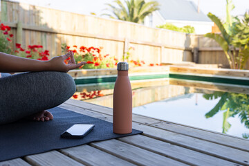 Meditating by pool, person practicing yoga with smartphone and water bottle nearby
