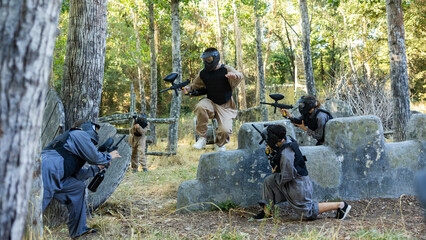 Skillful paintball team in protective outwear and helmets attacking hostile positions, running and...
