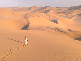 The girl walking on the top of the huge dune in Kumtag desert in Xinjiang, China, drone shot