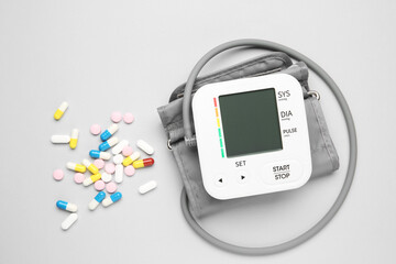 Blood pressure measuring device and pills on light grey background, top view