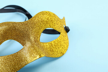 One golden carnival mask on light blue background, closeup. Space for text