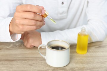 Young man dripping CBD tincture into drink at wooden table, closeup