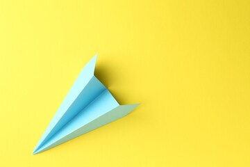 One handmade light blue paper plane on yellow background, top view. Space for text