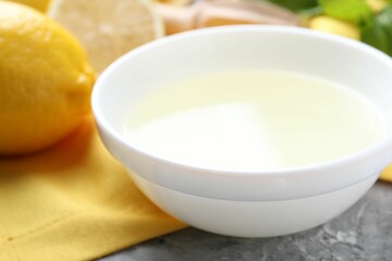 Fresh lemon juice in bowl and fruit on grey table, closeup