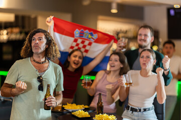 Group of friends fans watching match cheering with Croatian flag in bar