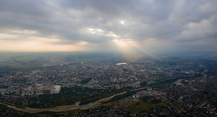 Aerial view from high altitude of distant city covered with puffy cumulus clouds flying by before rainstorm at sunset. Airplane point of view of landscape in cloudy weather
