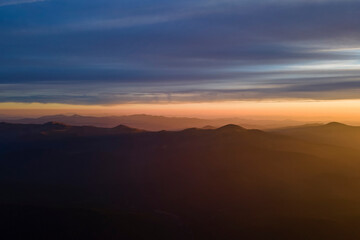 Aerial view of dark mountain hills with bright sunrays of setting sun at sunset. Hazy peaks and misty valleys in evening