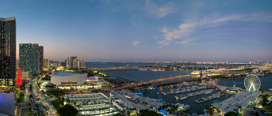 Aerial view of Skyviews Miami Observation Wheel at Bayside Marketplace with reflections in Biscayne Bay water and high illuminated skyscrapers of Brickell, city's financial center at night