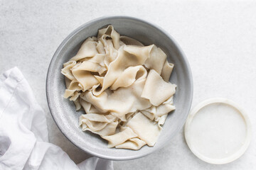 Overhead view of cooked hand pulled belt noodles in a grey bowl, top view of biang biang noodles on a marble countertop, process of making biang biang mian