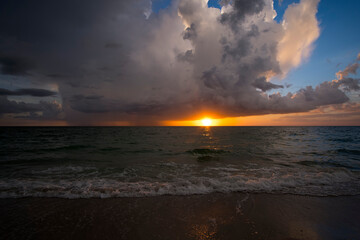 Sunset landscape of rainstorm with lightning and thunder over sea water waves crushing on sandy beach. Beautiful seascape in evening
