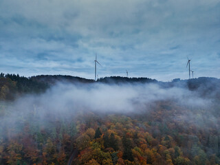 Fototapeta premium The shot of wind turbines standing on a hill in an autumn tendon with fog on the slope
