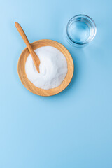 水色背景に木の器にはいった重曹とコップの水の俯瞰