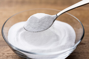木目テーブルに置かれたガラスの器から重曹の粉をスプーンですくう