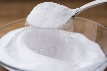 木目テーブルに置かれたガラスの器から重曹の粉をスプーンですくう