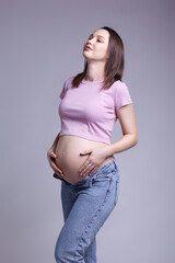 Young pretty pregnant woman in pink t-shirt and jeans on gray background.