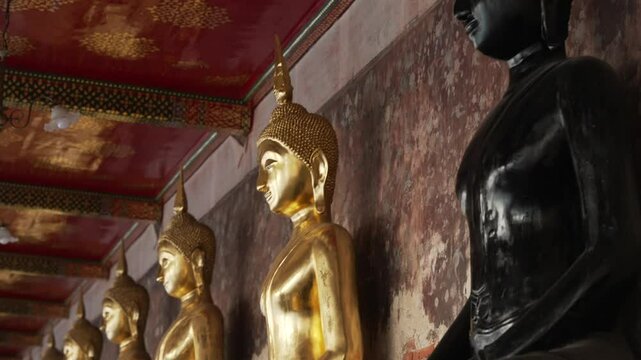A row of many statues of a gold Buddha and black one among, sitting in a meditative pose in the courtyard of a Buddhist temple Wat Pho. The most visited tourist place in Bangkok, Thailand