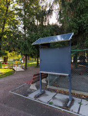 A sign on a sidewalk in a park with a bench and a fence