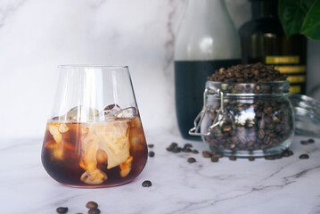 a glass of homemade iced cold brew coffee with milk on white marble table.