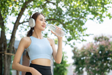 Happy slim woman drinking water after workout exercising in the city at sunrise. Young beautiful asian drinking water after jogging running outdoor. Healthy and active lifestyle concept.