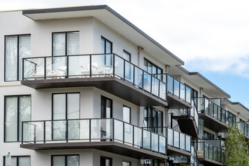 Modern residential white apartment building features glass balconies and contemporary architectural design. Urban residential development of multiple units with outdoor living spaces.