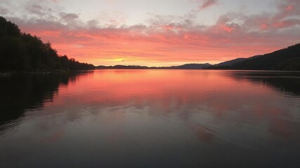 Fototapeta premium Vivid orange and pink hues reflecting on calm waters of Hintersee lake during autumn sunset, nature, reflection, sky