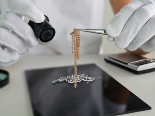 Obraz premium Jewelry appraiser examining a delicate gold chain with precision tools in a well-lit office